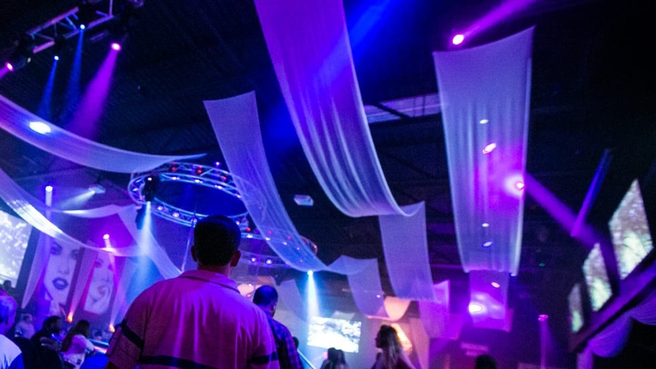 White ceiling drapes lit purple and blue over the main floor, a guest standing in the foreground