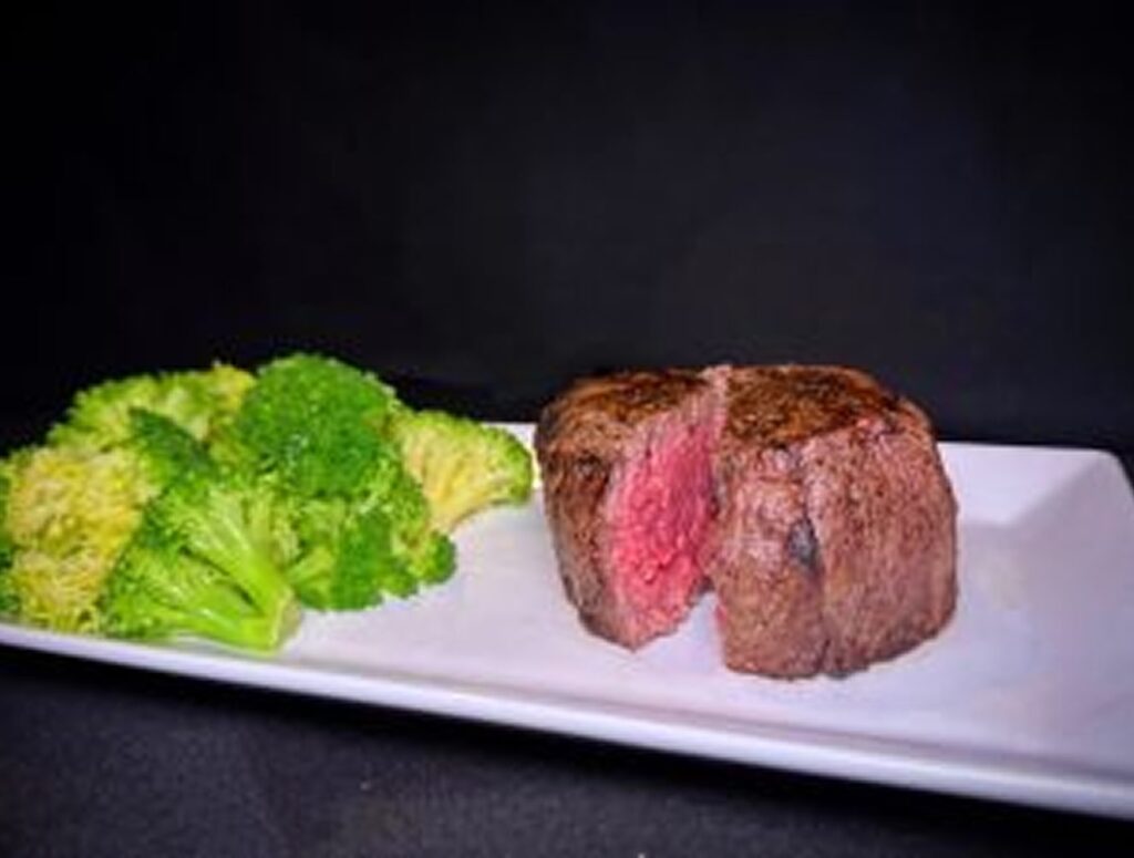 Juicy grilled steak served with fresh broccoli on a white plate.